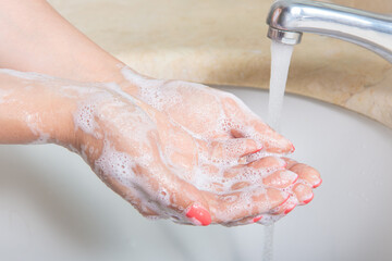 Fototapeta premium Woman Washing hands to prevent spread of CoronaVirus as well as cold, flu, bacteria at home. Woman use soap and washing hands under the water tap. Hygiene concept hand detail.