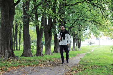 Fototapeta premium A young man in glasses walks in the park with an umbrella during the rain.