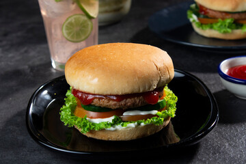 Delicious fresh meat burgers with tomato sauce and vegetables on a dark background.
