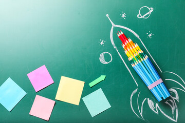 Creative composition with drawn space rocket and stationery on chalkboard