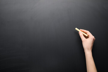 Female hand with piece of chalk on blackboard - obrazy, fototapety, plakaty