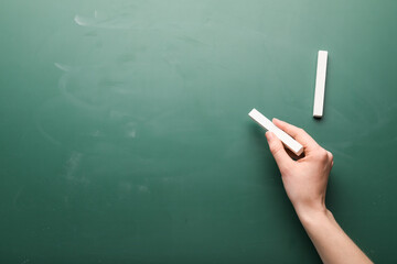 Female hand with pieces of chalk on blackboard