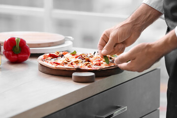 Mature male chef cooking tasty pizza in kitchen, closeup
