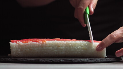 Chef cutting rolls of sushi with a knife on a stone board. - shot at a low angle. Beautiful female hands cut sushi.