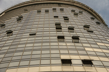 Bottom view of a multi-storey building against the sky with several open windows on the mirrored facade.