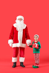 Cute little elf with Santa Claus and Christmas gift on color background