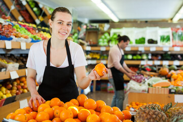 Young woman wearing apron working with fresh oranges on the supermarket