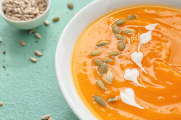 Tasty pumpkin cream soup in bowl on color background, closeup
