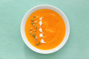 Tasty pumpkin cream soup in bowl on color background