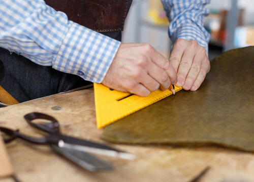 Male hands using triangular ruler for measuring and cutting leather for upholstering vintage chair