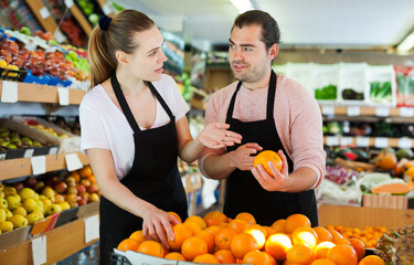 Young male and woman standing and holding fresh oranges in fruit store