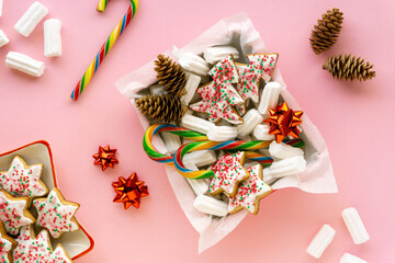 Christmas or new year gift box with gingerbread cookies, marshmallows and lollipops on a pink background