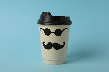 Paper cup with painted mustaches and glasses on blue background