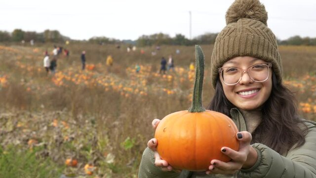 Happy woman in warm clothes holding her pumpkin and smiling while at a pumpkin patch