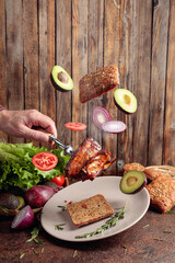 Grilled meat with flying slices of onion, avocado, and tomato.