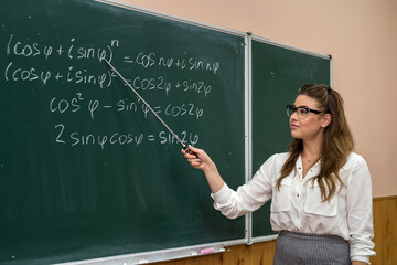 Young teacher writing and explain the mathematical formulas on a chalkboard