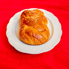 tsoureki, traditional Greek sweet bread served on white plate and red fabric background