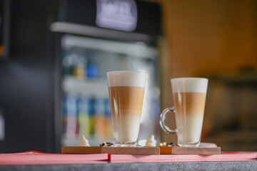 Coffee latte in two tall glasses on table in a bar with blurred background.