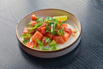 Watermelon salad with feta, fresh greenery and lime served in a unique shaped plate over black wooden table.