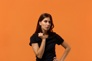 Obraz premium I was deceived. Curious cheerful caucasian woman in black t-shirt holds fist near face, overhears interesting conversation, feels cheated. Isolated over an orange wall