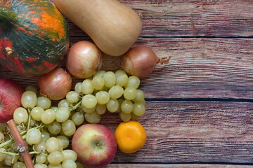 Autumn composition with pumpkin, onion, apple, tangerine and grapes on wooden background