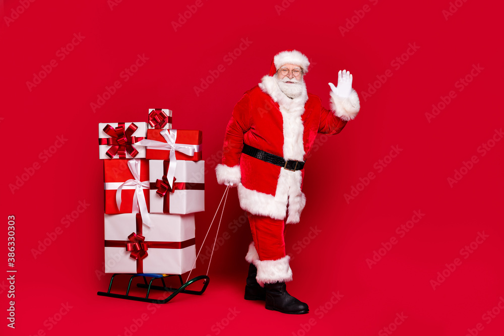 Wall mural photo portrait of funky white bearded man in santa claus costume pulling stack of presents on sleigh