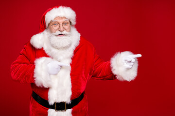Photo of retired grandpa grey beard direct finger empty space suggest curious newyear product wear santa costume leather belt gloves coat spectacles headwear isolated red color background