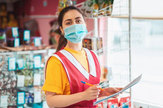 Food store. Portrait of a female employee in uniform with a medical mask on her face, holding documents. The concept of protecting against coronavirus at work