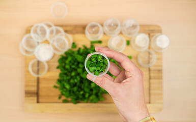 Man putting fresh chive leaves intro plastic containers to freeze.