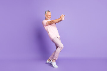 Fototapeta na wymiar Full length profile photo of pensioner man close fingers gun play wear pink t-shirt pants sneakers isolated purple color background