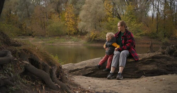 early fall in forest, people are walking at good weather, mother and child are sitting on shore of river