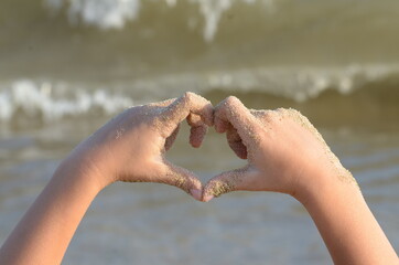 Hands of a child making a heart, sea waves on the background