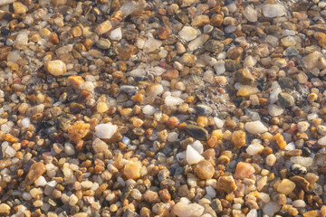 Small brown stones are washed by sea water. Stone background. Sea shore. Pebble beach.