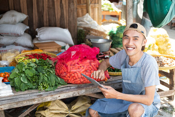 close up of the man selling the vegetable stall smiling while using the tablet pc in the vegetable stall background