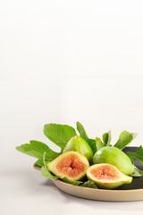 Brown plate of whole figs and halved with fig leaves and white background. Vertical arrangement