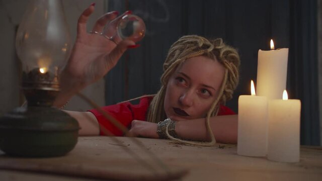 Lovely mysterious female psychic with dreadlocks in trance state, scrying vision of the future with crystal ball while seer crystal gazing during seance of clairvoyance in rustic house.