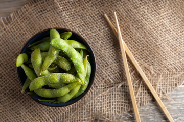 Japanese appetizer Edamame green soybeans seasoned with salt in a bowl, with shop sticks on the side.