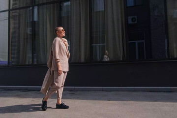 A woman with short hair in gray coat and glasses dancing, walking, smiling on a city street.