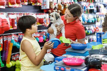 Portrait of small boy with mother and little dog choosing accessories for pet in shop