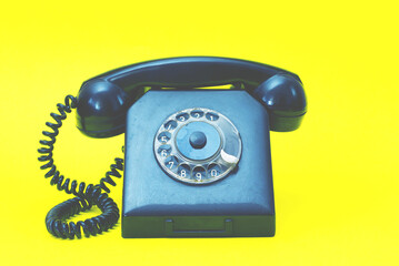 A vintage landline telephone in blue and yellow colors. A retro style dial phone on yellow background.