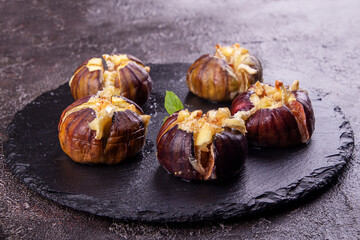 Ripe figs baked with cow's-milk cheese brie and camambert and sprinkled with bread crumbs decorated with mint leaves  on black stone background. Healthy eating concept. top view
