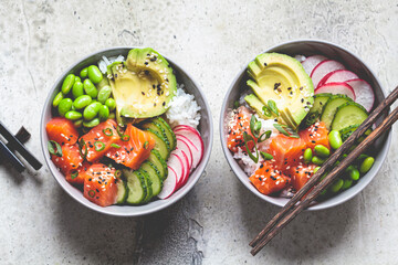 Poke bowl with salmon, rice, avocado, edamame beans, cucumber and radish in a gray bowls, top view. Hawaiian ahi poke bowl, gray background.