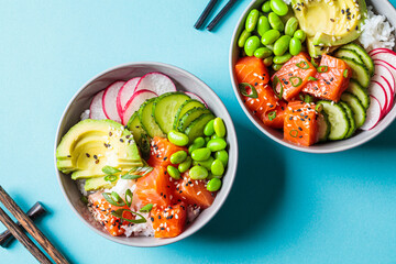 Poke bowl with salmon, rice, avocado, edamame beans, cucumber and radish in gray bowls, top view....
