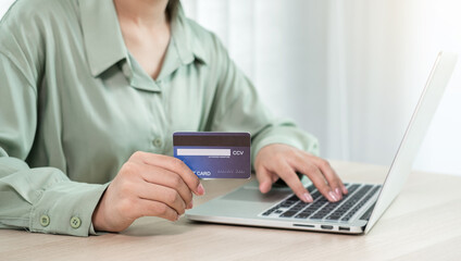 The businesswoman's hand is holding a credit card and using a laptop for online shopping and internet payment in the office