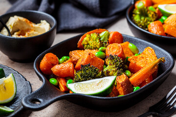 Baked vegetables in cast iron pans, dark background. Baked sweet potatoes, broccoli, carrots, and beans.