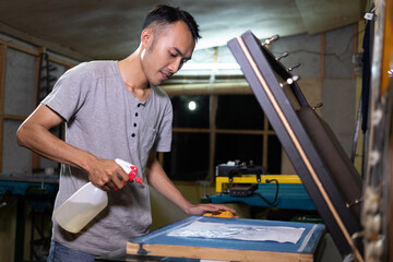 Male worker using sprayer to to paste the paper when going to make a film on the silkscreen