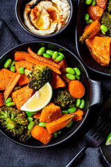 Baked vegetables in cast iron pans, dark background, top view. Baked sweet potatoes, broccoli, carrots, and beans.