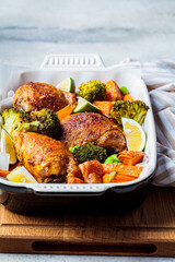 Baked chicken with vegetables in black dish, gray background, vertical.