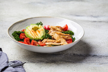 Chicken salad with tomato, avocado and kale in gray bowl. Diet food concept.