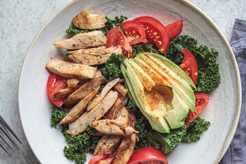 Chicken salad with tomato, avocado and kale in gray bowl, top view. Diet food concept.